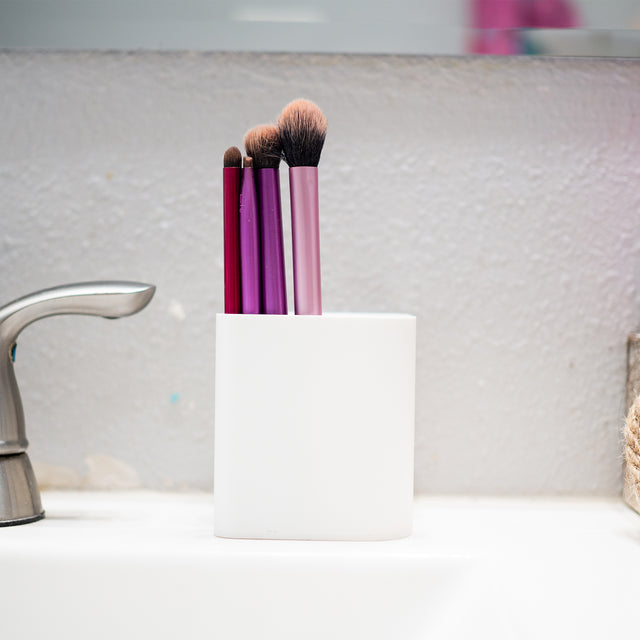 a close up of three brushes in a cup on a sink